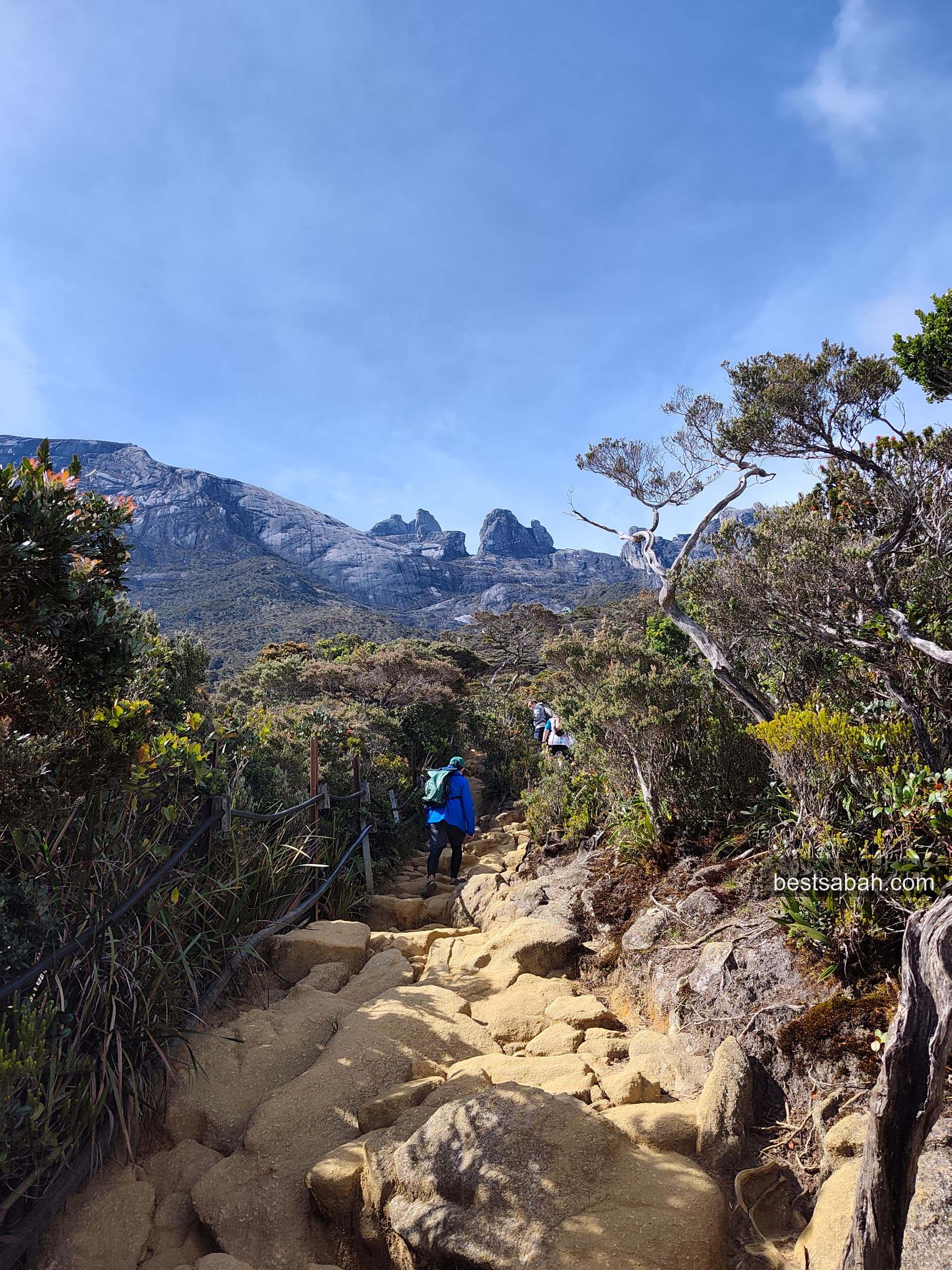 Hiker on the trail below Kinabalu's granite pinnacles under blue sky