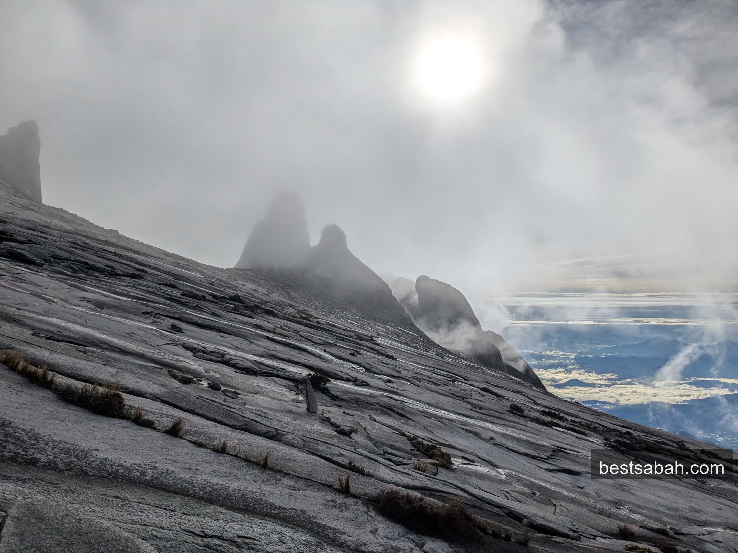 Granite spires of Mount Kinabalu emerging through cloud with a sun halo at sunrise
